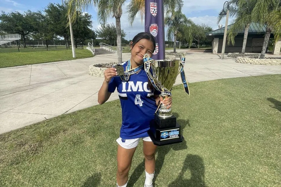Pemain Singapura, Irsalina Irwan, memegang trofi kejuaraan Piala Negeri Persatuan Bola Sepak Belia Florida (FYSA) bagi musim 2023-24 bersama pasukan Perdana Bawah 19 Tahun (U-19) Perempuan Akademi IMG pada 29 April.