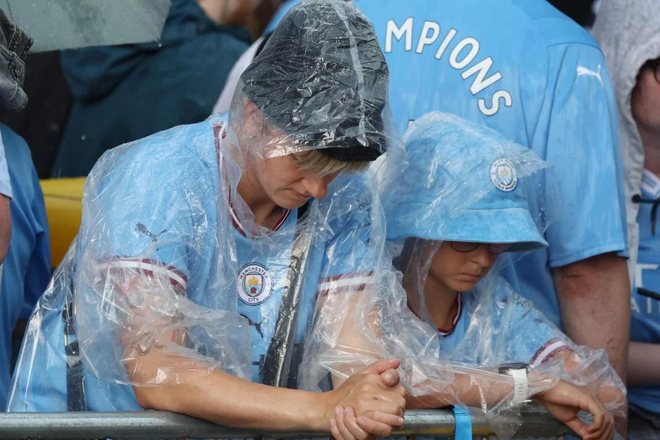 HUJAN? TIDAK MENGAPA: Dua penyokong Manchester City ini memakai baju hujan sementara menanti perarakan pasukan kesayangan mereka di kota Manchester. Perarakan itu tergendala sebentar kerana hujan lebat, tetapi diteruskan juga kerana ribuan penyokong City telah menanti di tepi jalan selama beberapa jam. 