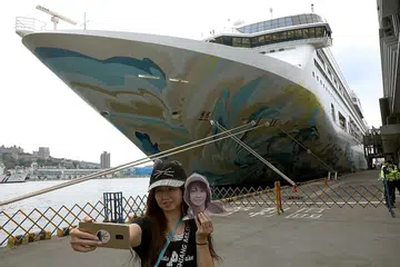 LAWATAN KE PULAU-PULAU: Seorang wanita mengambil gambar dirinya di depan kapal pesiaran Explorer Dream di Keelung kelmarin (gambar atas). - Foto REUTERS