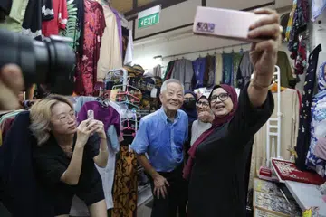 DEKATI MASYARAKAT: Encik Ng Kok Song (tengah) bergambar dengan pegerai dan pengunjung Pasar Geylang Serai semasa membuat lawatan ke sana pada Khamis.