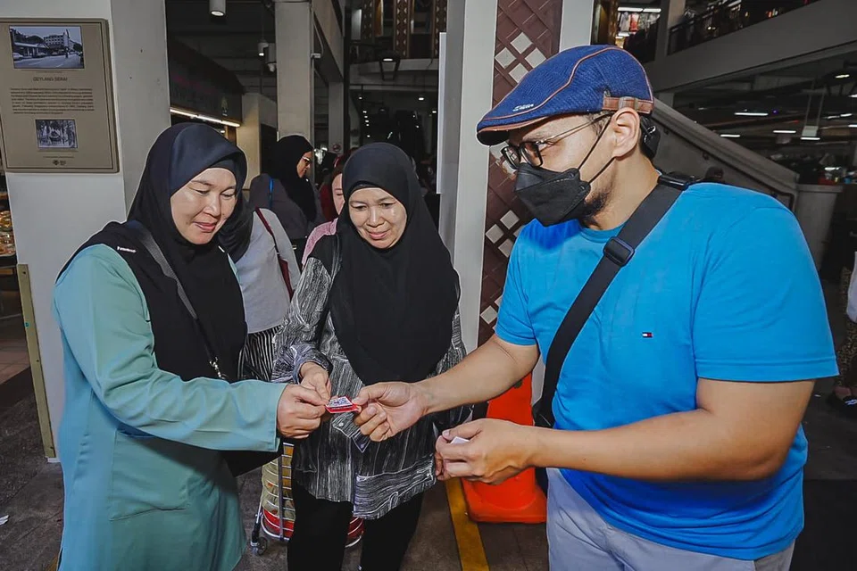 Pemilik laman geylangserai.shop, Encik Mohamed Fahmi Abdullah (kanan), mengagihkan kad nama yang memaparkan kod QR untuk laman tersebut di perkarangan Pasar Geylang Serai, dari 25-28 Julai. 
