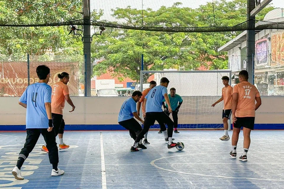 Pasukan Berita Harian (BH) (jersi biru, seluar hitam) bertarung di gelanggang futsal semasa satu kejohanan futsal Piala Sepanjang Hayat yang diadakan di 200 Woodlands Industrial Park E7 pada 29 September 2024. 