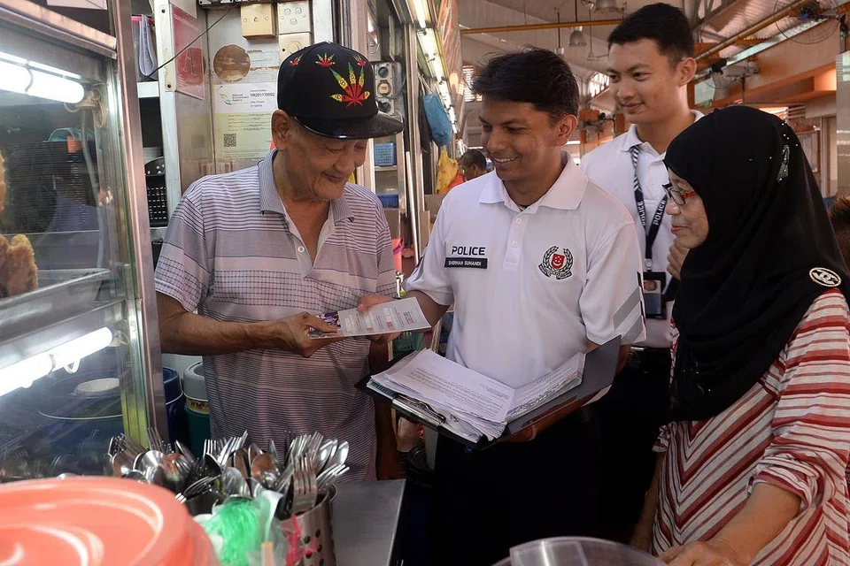 MENYEBARKAN RISALAH KEPADA PENDUDUK DAN PENIAGA DI KAWASAN CHONG PANG: Sarjan (NS) Sherhan (tengah) gigih melakukan tugasnya sebagai pegawai Penglibatan Masyarakat sambil mengedarkan risalah kepada pembantu gerai Encik Abu Bakar Othman dan Cik Koriyah Ashary. - Foto TAUFIK A. KADER