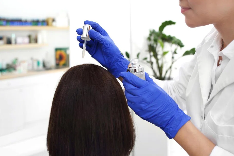 Pakar dermatologi menggunakan ubat pada kulit kepala wanita.