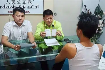 Encik Choo (membelakangkan kamera) menjelaskan tindakannya hendak menjadi gigolo kepada Encik Sim Chon Siang (berkemeja hijau). 