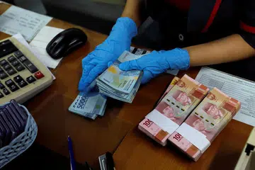 ELAK JANGKITAN: Seorang kakitangan memakai pelitup dan sarung tangan getah semasa mengira wang Rupiah di pejabat tukaran mata wang demi mencegah penularan koronavirus di Jakarta. 