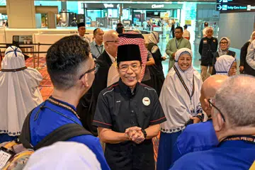 Menteri di Pejabat Perdana Menteri, Dr Mohamad Maliki Osman (baju hitam), beramah mesra dengan para jemaah haji dan keluarga mereka di Lapangan Terbang Changi pada 3 Jun.