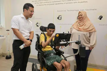 INTERAKSI BERSAMA: Encik Muhammad Sayfullah Mohamad Sahrin (tengah) berkomunikasi dengan Menteri Pembangunan Negara, Encik Desmond Lee, menggunakan alat komunikasi augmentatif dan alternatif sambil diperhatikan ibunya, Cik Siti Fadillah Mohamed Noor. Mereka menyertai acara National CARECarnival yang diadakan di Enabling Village di Lengkok Bahru pada Sabtu.