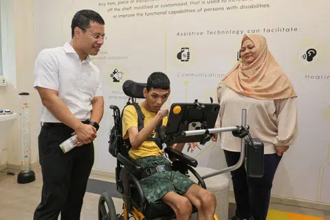INTERAKSI BERSAMA: Encik Muhammad Sayfullah Mohamad Sahrin (tengah) berkomunikasi dengan Menteri Pembangunan Negara, Encik Desmond Lee, menggunakan alat komunikasi augmentatif dan alternatif sambil diperhatikan ibunya, Cik Siti Fadillah Mohamed Noor. Mereka menyertai acara National CARECarnival yang diadakan di Enabling Village di Lengkok Bahru pada Sabtu.