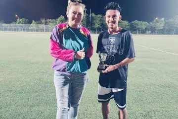 ANJUR LIGA BOLA DEMI SOKONG SUAMI: Penganjur liga Cik Nurul Natasha, 37 tahun (kiri) menghulurkan trofi kepada pemain terbaik Muhammad Azrin, 26 tahun (kanan).