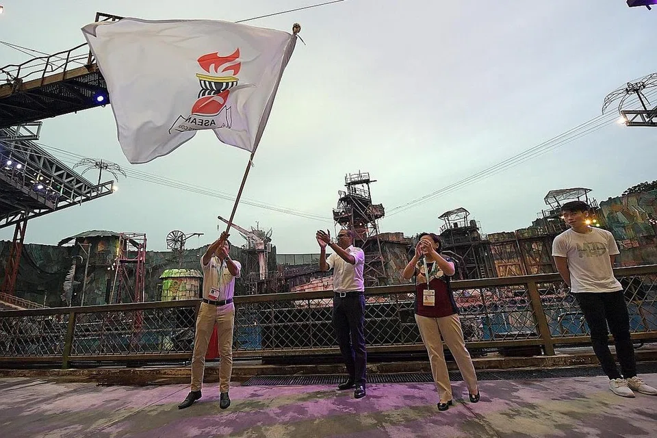 JUMPA LAGI DI MALAYSIA: Wakil Malaysia, Encik Zainal Abas (kiri),mengibarkan bendera Majlis Sukan Sekolah-Sekolah Asean, selepas menerimanya daripada Dr Janil (tengah), dengan diperhatikan Cik Tan, di majlis penutup ASG yang berlangsung di Universal Studios Singapore pada Khamis lalu.