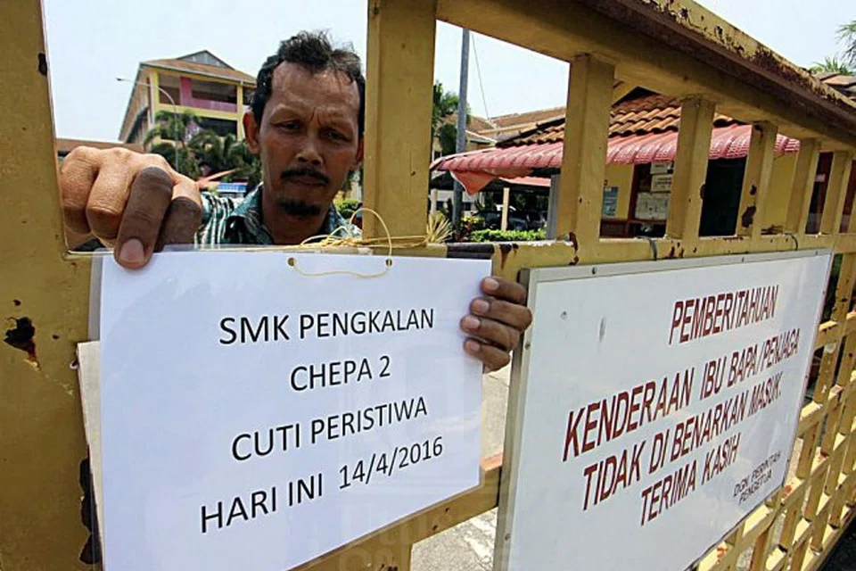 GARA-GARA HISTERIA: Seorang kakitangan Sekolah Menengah Kebangsaan (SMK) Pengkalan Chepa 2 menunjukkan papan tanda sekolah ditutup kerana keadaan histeria di sekolah itu. - Foto fail UTUSAN MALAYSIA