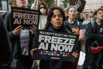 Penunjuk perasaan memegang sepanduk bertulis ‘We Didn’t Elect Big Tech, Freeze AI Now’ (“Kami tidak memilih syarikat teknologi gergasi, hentikan pembangunan AI sekarang.”) ketika menyertai perhimpunan membantah kecerdasan buatan (AI) di luar bangunan yang menempatkan pejabat OpenAI di SoHo, New York, pada 20 Oktober 2026. New York kini memperkenalkan undang-undang baru yang melarang chatbot AI bertindak sebagai teman peribadi kepada pengguna bawah 18 tahun, selain mewajibkan pengesahan usia bagi melindungi kanak-kanak dan remaja daripada risiko pergantungan emosi terhadap teknologi tersebut.