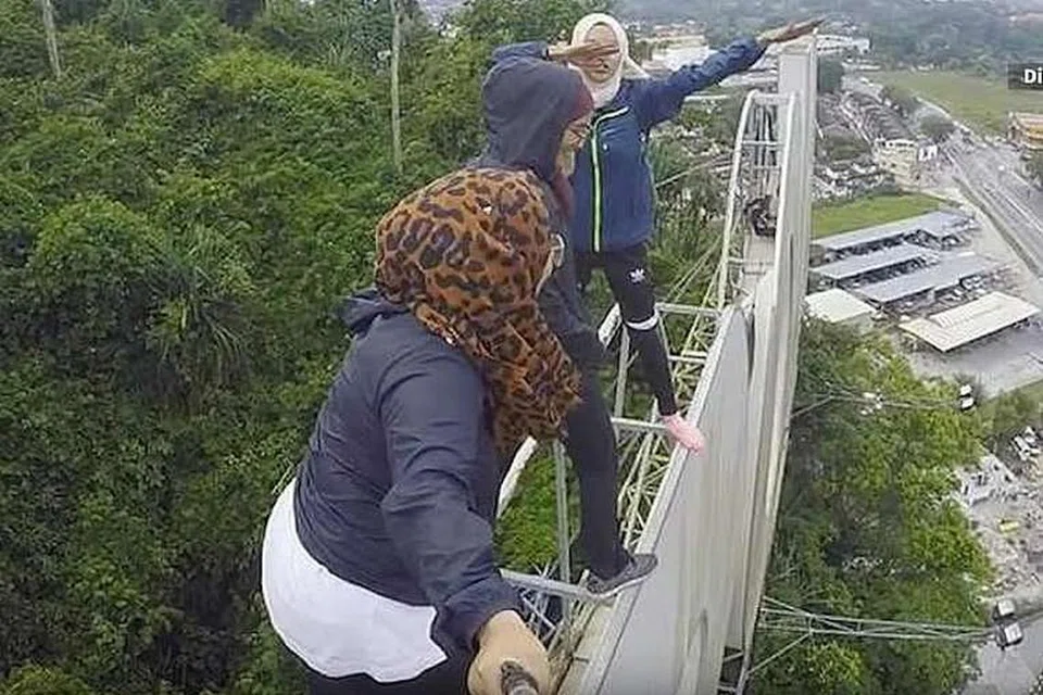 Lapan anak muda, termasuk tiga wanita, memasang buaian pada tanda gergasi 'IPOH' dan mengambil gambar menggunakan dron. Mereka kelihatan tidak memakai alat keselamatan. 