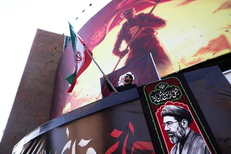 Seorang lelaki memegang bendera Iran bersebelahan gambar Pemimpin Tertinggi Iran, Ayatollah Mojtaba Khamenei, di Teheran pada 13 Ogos 2026. Tempoh 60 hari yang diberikan kepada Iran dan Amerika Syarikat untuk merundingkan perjanjian muktamad berakhir pada 17 Ogos tanpa penyelesaian, dengan kedua-dua pihak masih berselisih mengenai pembukaan semula Selat Hormuz, sekatan ekonomi dan program nuklear Teheran.
