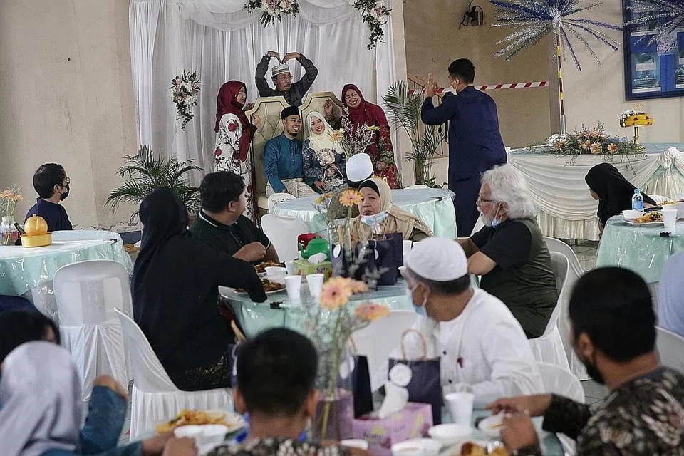 MERAIKAN PERKAHWINAN: Pengantin baru Cik Nadhirah dan Encik Muhd Faruq bergambar dengan anggota keluarga sambil tetamu menikmati makanan di majlis persandingan di kolong blok di Tampines semalam. - Foto BH oleh KEVIN LIM