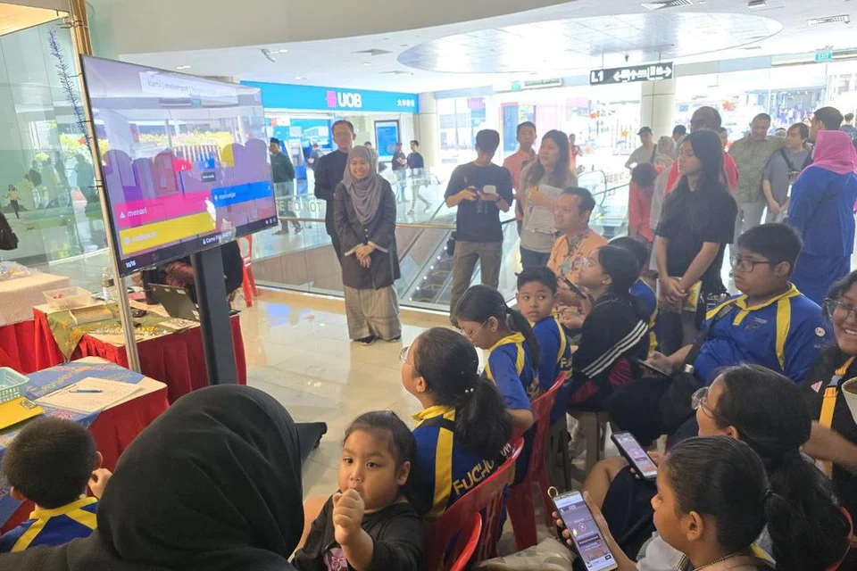 Encik Zaqy (berbaju oren) bersama beberapa pelajar dari Sekolah Rendah Fuchun bermain permainan dalam talian seerti-seiras dan kata berlawanan.