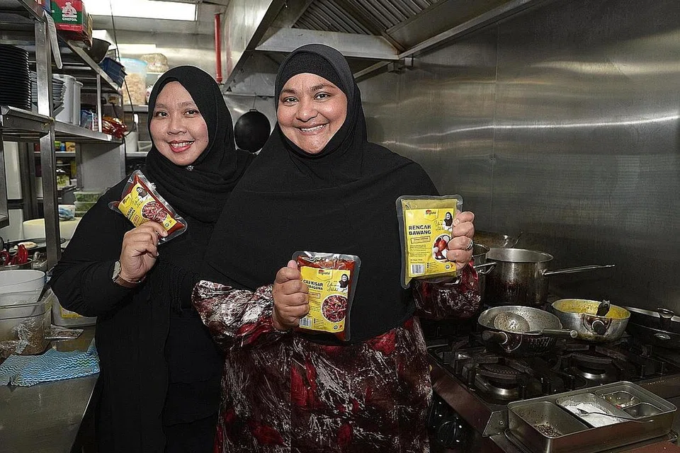 GANDINGAN MANTAP: Cik Ummi (kanan) dan Cik Norhuda dari Asyura bekerjasama untuk menghasilkan pes sambal asas cili kisar serba guna dan rencah bawang yang sudah dimasak. - Foto BH oleh SHINTARO TAY