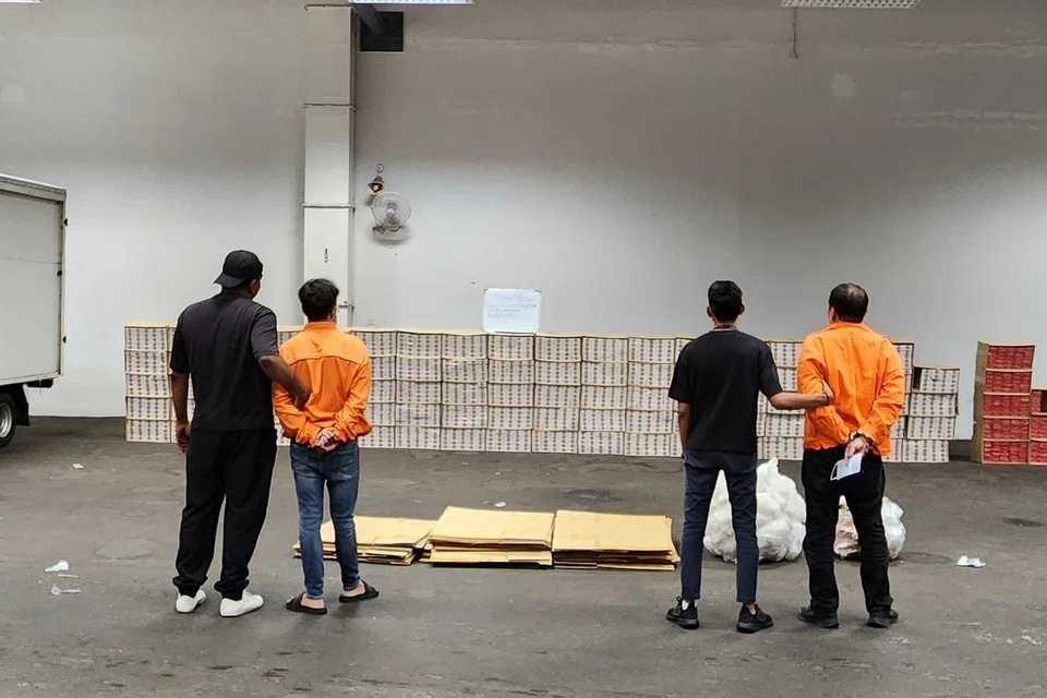 PADAH ELAK CUKAI: Dua lelaki ini (berpakaian oren) ditangkap dan 3,550 karton rokok tidak dibayar cukai serta sebuah trak dan sebuah van yang digunakan dalam kegiatan melibatkan barang elak cukai dirampas Kastam Singapura dalam satu operasi pada 2 Februari. - 
