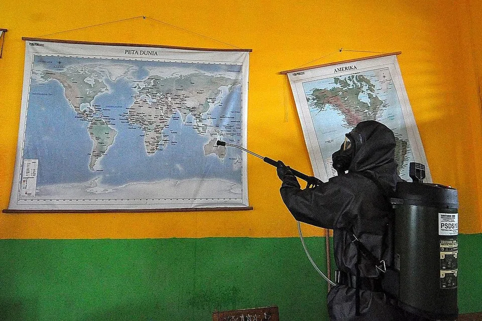 BERSIHKAN SEKOLAH: Seorang pegawai polis sedang menyembur cecair nyahkuman di sebuah sekolah di Palu, Sulawesi Tengah, dalam usaha mencegah penularan Covid-19 di negara itu. - Foto AFP