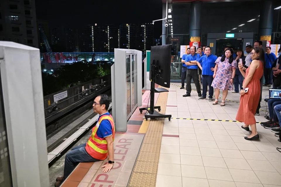Seorang lelaki menunjukkan bagaimana sistem pengesanan pencerobohan landasan di sistem LRT Sengkang-Punggol boleh mengesan orang yang duduk di hujung platform. Semua 28 stesen di LRT Sengkang-Punggol akan dilengkapkan dengan sistem pengesanan. Turut hadir di sesi demonstrasi itu ialah Anggota Parlimen (AP) GRC Pasir Ris-Punggol, Cik Yeo Wan Ling, (dua dari kanan).