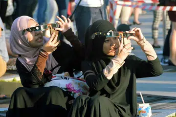 SAKSIKAN FENOMENA: Cik Nur Humairah (kiri) dan Cik Siti Hawa antara ribuan orang yang menyaksikan gerhana matahari di Pusat Sains Singapura semalam.
