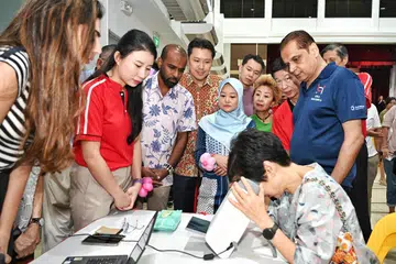 Penasihat Organisasi Akar Umbi GRC Jurong, Dr Hamid Razak (tiga dari kiri) dan Encik Shawn Huang (empat dari kiri); Setiausaha Parlimen Kanan (Kesihatan merangkap Undang-Undang), Cik Rahayu Mahzam (bertudung biru) dan Menteri Kemampanan dan Sekitaran, Cik Grace Fu (duduk, mengguna alat pemeriksaan) menyertai pemeriksaan penglihatan di satu reruai semasa Karnival EmpowerHER di Kelab Masyarakat Yuhua.