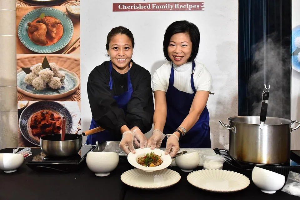 BUKU RESIPI: Pengerusi Sayap Wanita PAP, Cik Sim Ann (kanan) menyajikan biji abakus Hakka dengan penyumbang resipi, Cik Chan Wai Lin. Ini merupakan salah satu resipi dalam projek buku resipi Cherished Family Recipe Collection' (Koleksi Resipi Keluarga yang Dihargai) di Singapore Flyer pada Sabtu. - Foto PAP