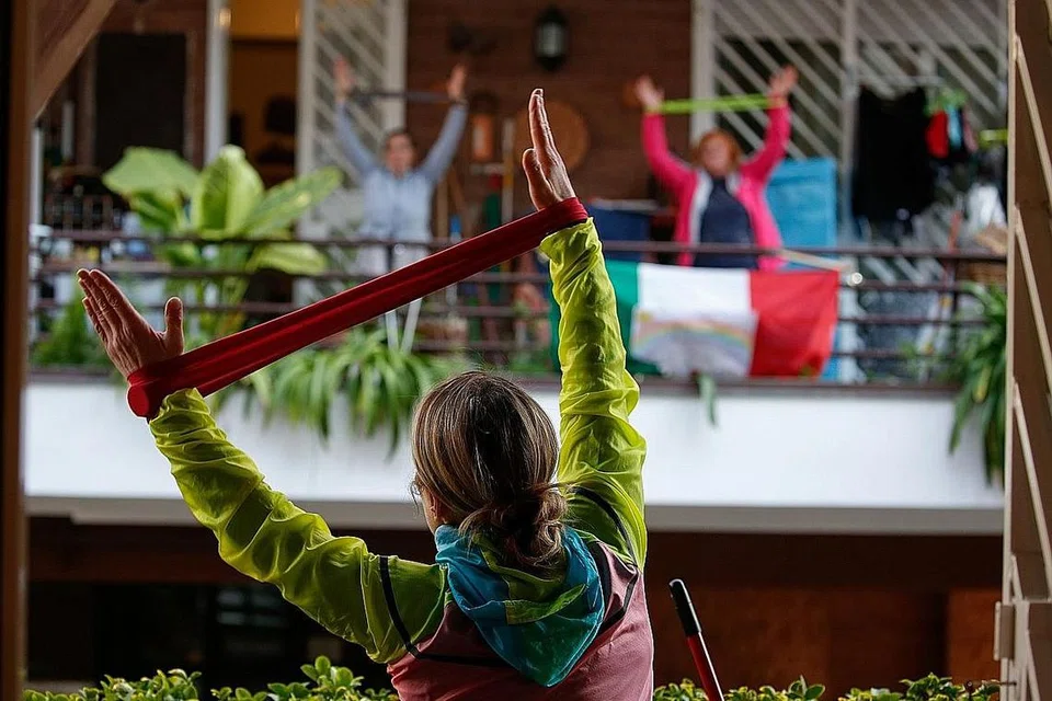DI ROME - KEKAL AKTIF: Instruktor kecergasan Antonietta Orsini membimbing jirannya melakukan beberapa senaman dari balkoni rumah masing-masing kerana mereka tidak boleh keluar rumah dek perintah berkurung di Italy. - Foto REUTERS 