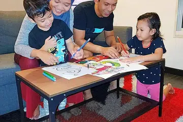 MEWARNA SAMBIL BELAJAR: Menurut Cik Ammirah, melalui cogan kata bertema setiap minggu, seperti 'StayHome SG', beliau dapat mewarna bersama suaminya, Muhammad Ridzman Rosli dan anak-anaknya, Adam Rizqullah Muhammad Ridzman (kiri) dan Rabiatul Adawiyah Muhammad Ridzman (kanan) serta memaklumkan mengapa mereka tidak dapat lakukan aktiviti yang biasanya dilakukan seperti bermain di taman permainan dan kepentingan untuk duduk di rumah. - Foto ihsan SITI AMIRAH SAHARI