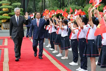 SAMBUTAN MESRA: Perdana Menteri, Encik Lee Hsien Loong, yang disambut oleh Perdana Menteri Vietnam, Encik Pham Minh Chinh, di Istana Presiden di Hanoi, melambai mesra kepada kanak-kanak yang memegang bendera Singapura dan Vietnam, tanda ikatan akrab kededua negara. 
