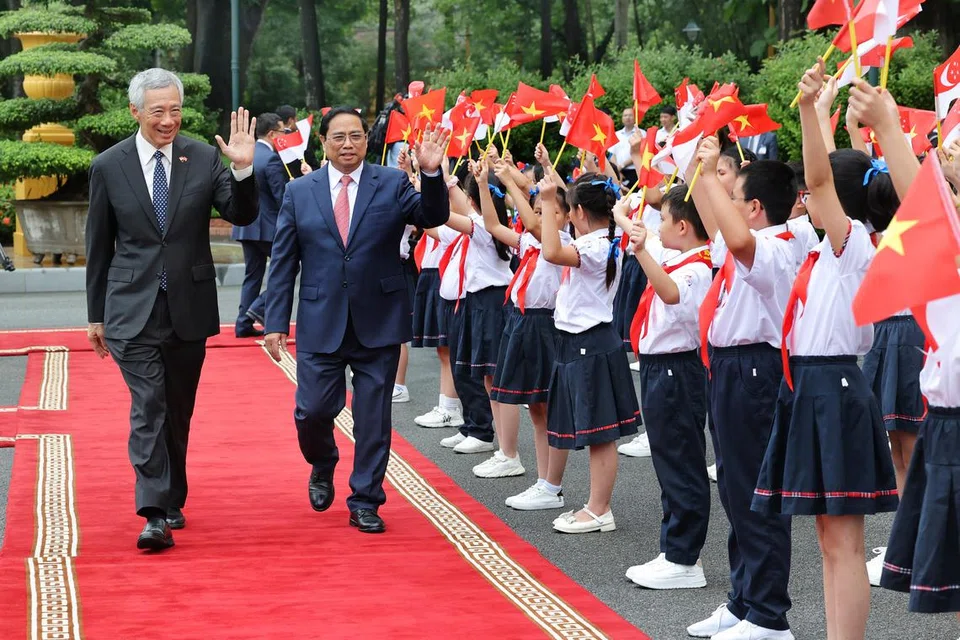 SAMBUTAN MESRA: Perdana Menteri, Encik Lee Hsien Loong, yang disambut oleh Perdana Menteri Vietnam, Encik Pham Minh Chinh, di Istana Presiden di Hanoi, melambai mesra kepada kanak-kanak yang memegang bendera Singapura dan Vietnam, tanda ikatan akrab kededua negara. 