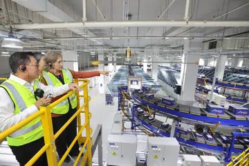 Menteri Penerangan dan Pembangunan Digital, Cik Josephine Teo (kanan), meninjau kemudahan pengasingan bungkusan automatik baru SingPost, ditemani Pengerusi, Cik Teo Swee Lian (terselindung); dan Ketua Pegawai Eksekutif (CEO), Encik Mark Chong, semasa pelancaran kemudahan tersebut di hab logistik e-dagang serantau SingPost di Tampines, pada 9 Jun.