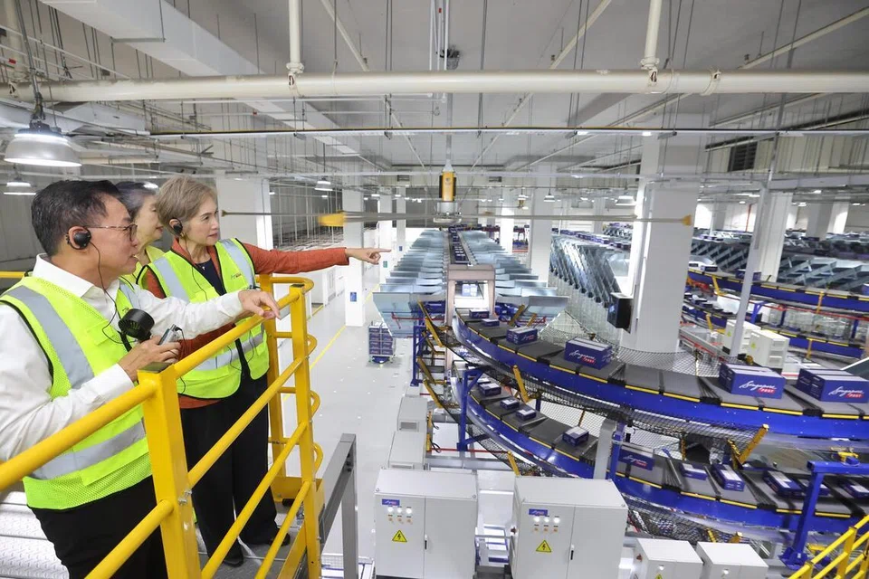 Menteri Penerangan dan Pembangunan Digital, Cik Josephine Teo (kanan), meninjau kemudahan pengasingan bungkusan automatik baru SingPost, ditemani Pengerusi, Cik Teo Swee Lian (terselindung); dan Ketua Pegawai Eksekutif (CEO), Encik Mark Chong, semasa pelancaran kemudahan tersebut di hab logistik e-dagang serantau SingPost di Tampines, pada 9 Jun.