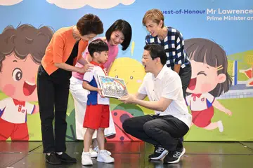 Perdana Menteri Encik Lawrence Wong (kanan) menerima tanda penghargaan daripada Hunter Tan Yi Ming, seorang pelajar K1 dari PCF Sparkletots Centre @ Cheng San - Seletar Blok 556. Bersamanya adalah Menteri Negara Kanan (Kebudayaan, Masyarakat dan Belia merangkap Perdagangan dan Perusahaan), Cik Low Yen Ling (kiri, berbaju oren); Menteri Negara (Ehwal Dalam Negeri merangkap Pembangunan Sosial dan Keluarga), Cik Sun Xueling (berbaju merah jambu); dan Menteri Penerangan dan Pembangunan Digital, Cik Josephine Teo (berbaju kotak-kotak).