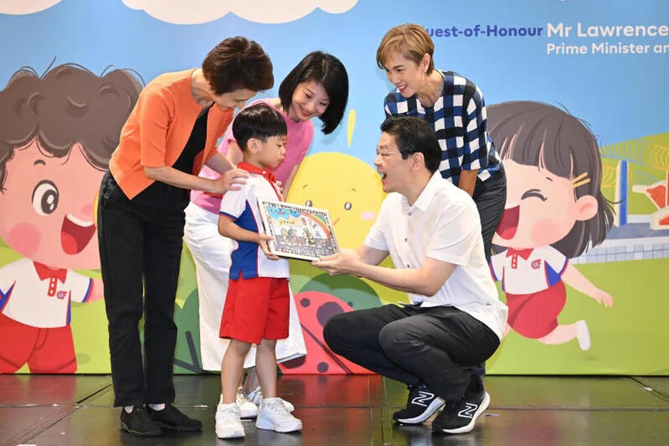 Perdana Menteri Encik Lawrence Wong (kanan) menerima tanda penghargaan daripada Hunter Tan Yi Ming, seorang pelajar K1 dari PCF Sparkletots Centre @ Cheng San - Seletar Blok 556. Bersamanya adalah Menteri Negara Kanan (Kebudayaan, Masyarakat dan Belia merangkap Perdagangan dan Perusahaan), Cik Low Yen Ling (kiri, berbaju oren); Menteri Negara (Ehwal Dalam Negeri merangkap Pembangunan Sosial dan Keluarga), Cik Sun Xueling (berbaju merah jambu); dan Menteri Penerangan dan Pembangunan Digital, Cik Josephine Teo (berbaju kotak-kotak).