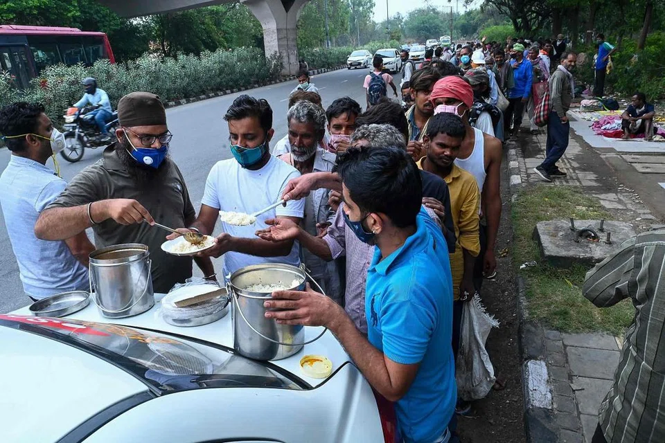 BEKALAN MAKANAN IHSAN: Golongan gelandangan dan pekerja bergaji rendah yang terjejas dek pandemik beratur mendapatkan bekalan makanan daripada sukarelawan di tepi jalan di ibu kota New Delhi pada 20 Mei lalu. - Foto AFP