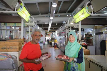DUA GERAI ADA E-PEMBAYARAN: Cik Rahima Beevi dan bapanya, Encik Mohd Faruk, mengendali dua gerai di Pasar Pek Kio. Cik Rahima pemilik gerai Tazmeen Beef Stall yang menjual daging lembu, manakala bapanya, pemilik gerai Faraz Ahmed Mutton Stall, menjual ayam dan daging kambing. Mereka berdua menawarkan kaeadah e-pembayaran kepada pelanggan.