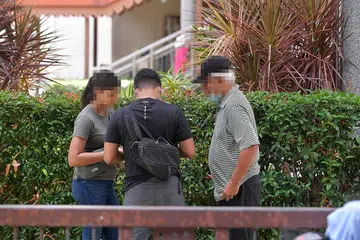 JALANKAN PEMERIKSAAN: Pegawai Kastam yang berpakaian preman memeriksa seorang individu di bawah jejambat lalu lintas Pasar Geylang Serai pada Sabtu lalu. - Foto BH oleh ALPHONSUS CHERN