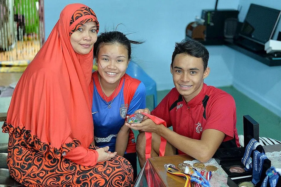 KEBANGGAAN KELUARGA: Suhairi menunjukkan pingat perak Sukan Para Asean (APG) kepada ibunya, Cik Subahariah Ponibi, dan adiknya, Suhartini Suhani.