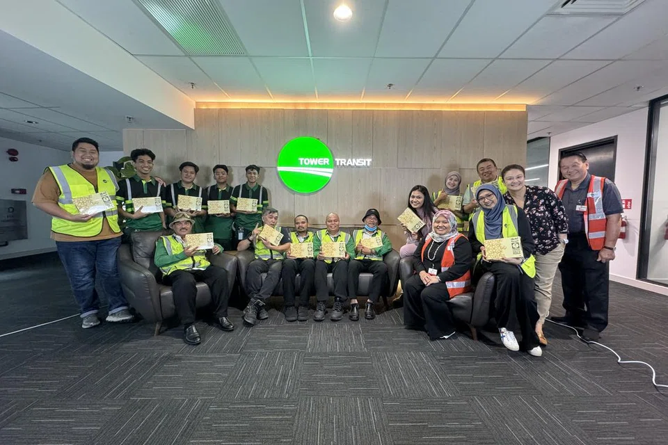 Pengarah Tamar Madinah, Cik Dewi Suhadi (duduk memakai vest keselamatan berwarna oren), menemui kakitangan perkhidmatan bas, Tower Transit Singapura (TTS) untuk mengagihkan kurma kepada mereka. 