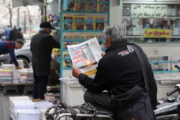 Seorang lelaki membaca akhbar yang memaparkan gambar peluru berpandu Iran sambil duduk di sebelah sebuah kedai buku di Teheran, Iran, pada 7 Februari. 