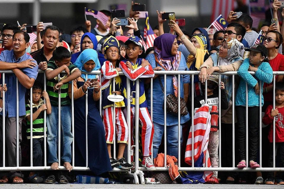 SEMANGAT PATRIOTIK: Warga Malaysia, ada dengan pakaian dengan warna bendera negara, menantikan perbarisan di tepi jalan raya di Putrajaya semalam. - Foto AFP 