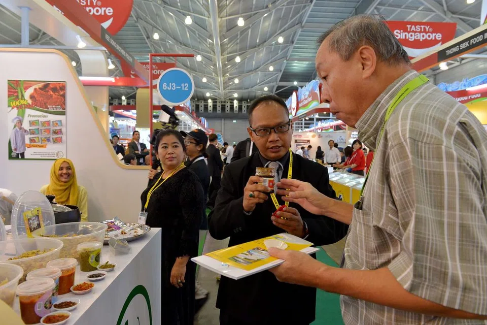 MENCUBA PRODUK: Encik Nor Hashim mengundang salah seorang pelawat ke Food and Hotel Asia 2016 mencuba makanan yang dihasilkan syarikatnya, Wahyu Delicacies Rempeyek Trading, yang antaranya rempeyek. - Foto TUKIMAN WARJI