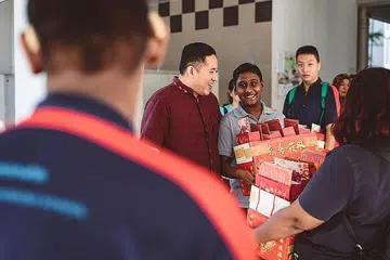 LIBATKAN PELAJAR: Pelajar dari beberapa sekolah rendah dan menengah ikut serta dalam kegiatan mengagihkan buah oren kepada penduduk di Woodlands bersama Setiausaha Parlimen Kanan (Ehwal Dalam Negeri merangkap Kesihatan), Encik Amrin Amin (berbaju merah). - Foto FACEBOOK AMRIN AMIN
