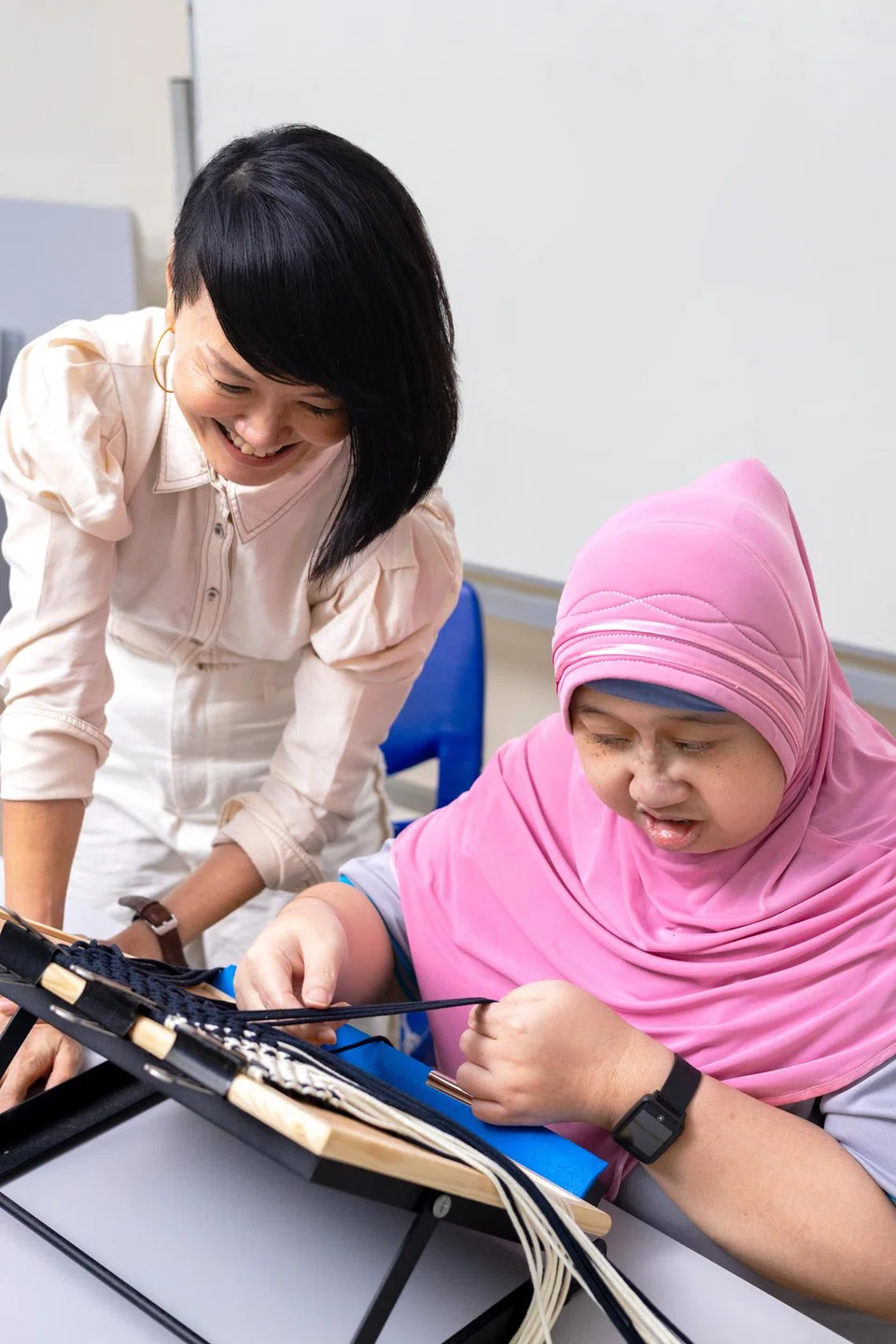 Cik Lu-Lyn Chang (kiri) mengajar klien Persatuan Golongan Kurang Daya Intelek Singapura (Minds), Cik Hidayah mengenai kaedah makrami iaitu simpulan untuk menghasilkan beg bagi koleksi inklusif mereka. 