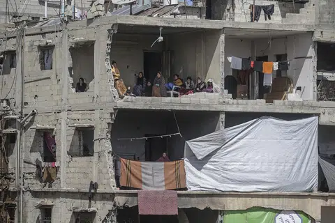 Sebuah keluarga Palestin duduk di dalam rumah yang rosak sambil memerhatikan usaha orang ramai mencari mayat dan mangsa terselamat di celah runtuhan sebuah lagi rumah (tidak kelihatan dalam gambar) milik keluarga Hattab selepas serangan udara oleh Israel di Bandar Gaza pada 19 Mac 2025. Menurut Kementerian Kesihatan Palestin di Gaza, serangan udara tersebut telah mengorbankan sekurang-kurangnya empat anggota keluarga Hattab.