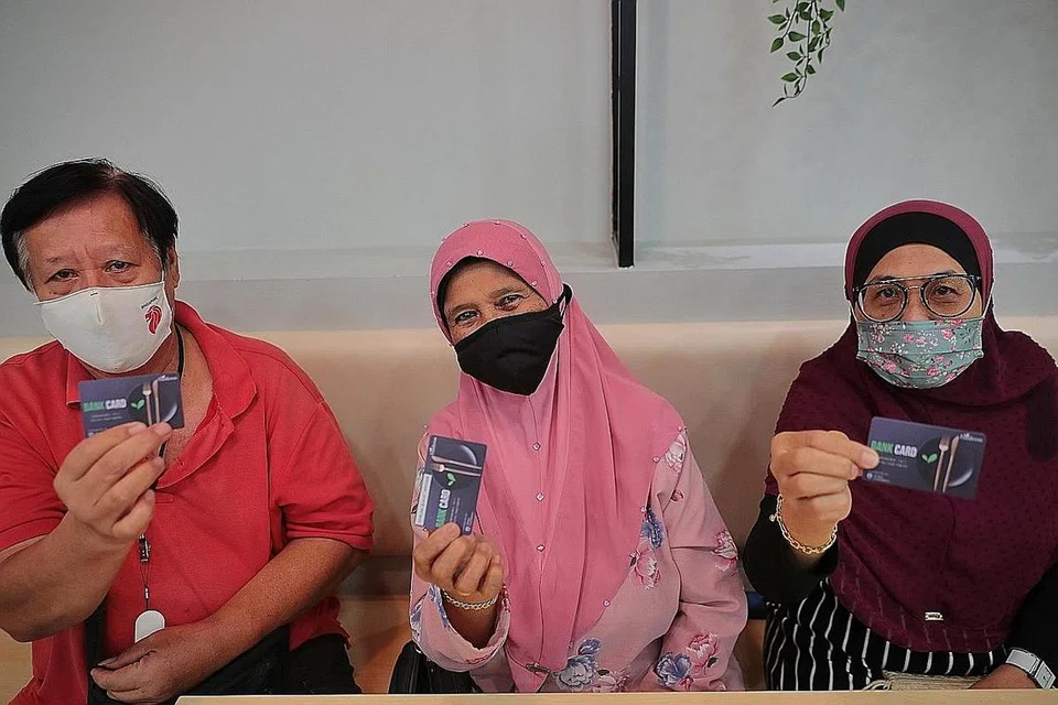 GEMBIRA DENGAN KAD BARU: (Dari kiri) Encik Othman Mustari, 70 tahun, Cik Norlini Mansor, 70 tahun dan Cik Mona Samin, 68 tahun, melahirkan perasaan gembira menerima kad bank FBSG yang diagihkan untuk inisiatif baru Tap-A-Meal. - Foto BH oleh JASON QUAH