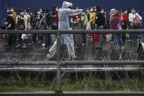 JALANI RAWATAN: Kakitangan Top Glove menunggu di luar kilang untuk dipindahkan ke hospital berdekatan asrama mereka di Setia Alam, di luar Kuala Lumpur, kelmarin. - Foto EPA-EFE