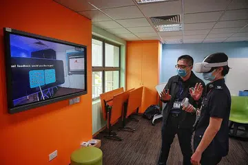 MANFAATKAN TEKNOLOGI REALITI MAYA: Jurulatih Besar, Komand Latihan Penguasa Imigresen dan Pusat Pemeriksaan (ICA), ASP Sophia Ng kelihatan sedang menjalani simulasi mengendali sebuah kelas Realiti Maya (VR) sambil menerima bimbingan oleh Eksekutif Kanan (Perancangan Kurikulum), Pusat bagi Sistem Pembelajaran Akademi Home Team, Encik Ian Koh. - Foto-foto BH oleh JASON QUAH